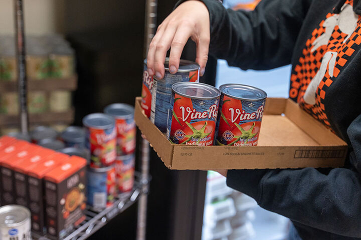 Close up of a woman's hand on a can of tomatoes as she stocks shelves in a food pantry.